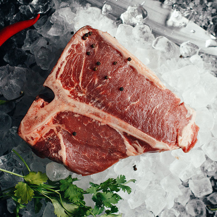 A beautifully marbled t-bone steak laying on a bed of ice with cilantro and peppercorn