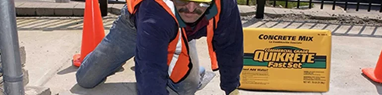 Man in hard hat and hi-vis vest smoothing out concrete with a bag of Quikrete beside him
