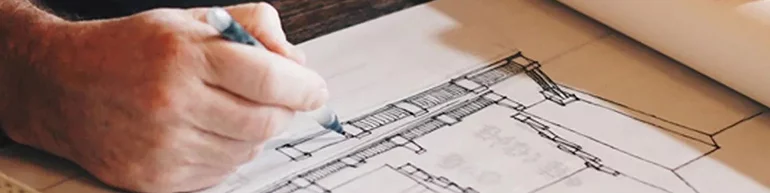 Person holding a pen looking over blueprints