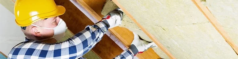 Man wearing a dust mask, work gloves and hard hat putting insulation in an attic
