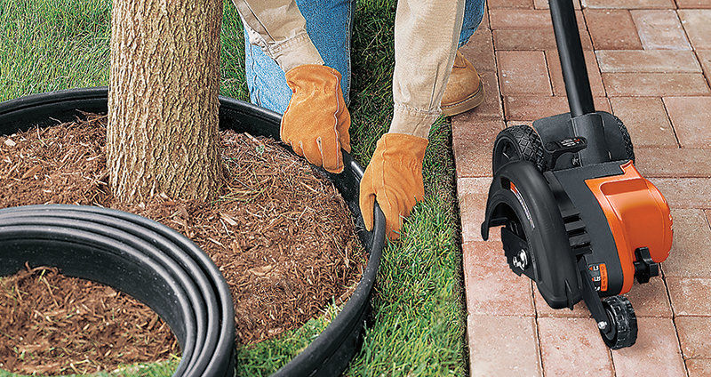 Person adding plastic landscape edging around a tree with brown mulch