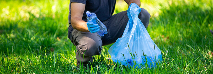 Man wearing blue latex gloves as he crouch down to put trash in a blue plastic bag