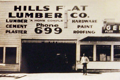 An old photo of a Hills Flat Lumber storefront location with a man standing in front