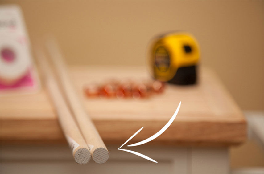 Two dowels cut sitting on a wooden countertop with a tape measure in the background