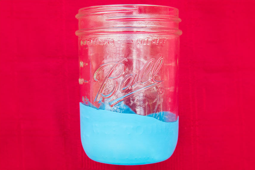 A mason jar sitting on a red background with a blue balloon stretched around the bottom 