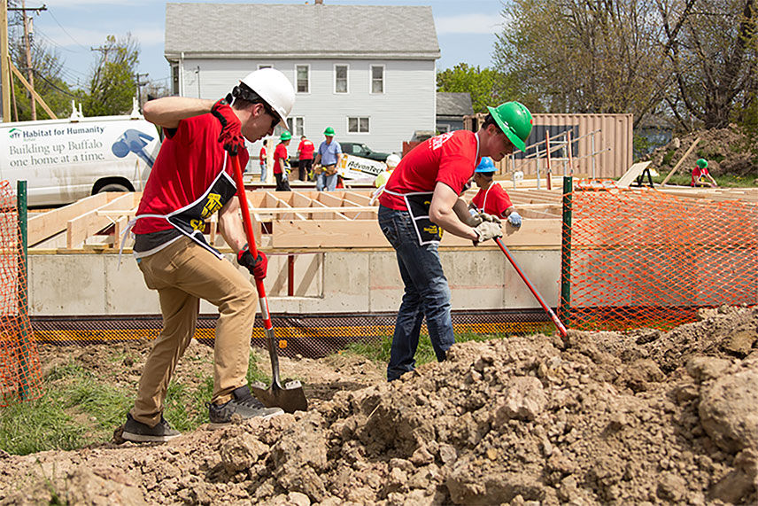 Two Valu crew members using shovels to dig near the home being built