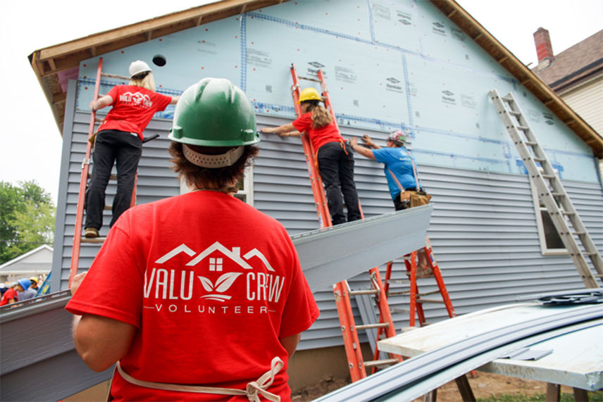 Women from the Valu Home Centers team installing siding on the house