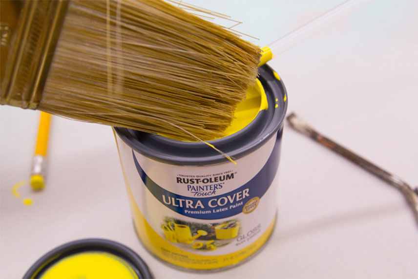 paint brush being dipped into a small can of yellow paint 