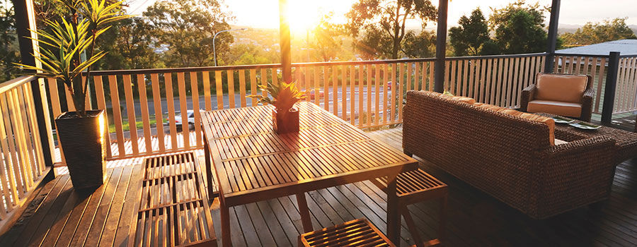A serene patio with wooden guard rail, patio furniture and plant accents overlooking a beautiful sunset