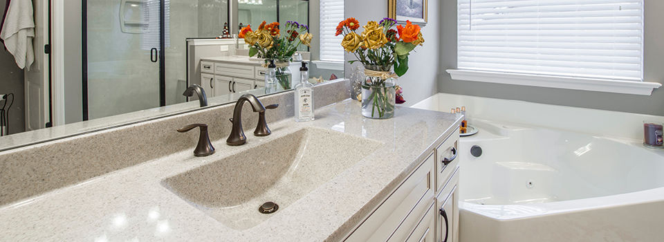 A bathroom vanity with flowers on the counter and bathtub in the corner