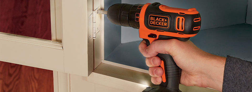 A person uses a Black & Decker 12V MAX 3/8 In. Cordless Drill to drive a screw into the inside edge of a cabinet frame, securing a hinge or bracket.