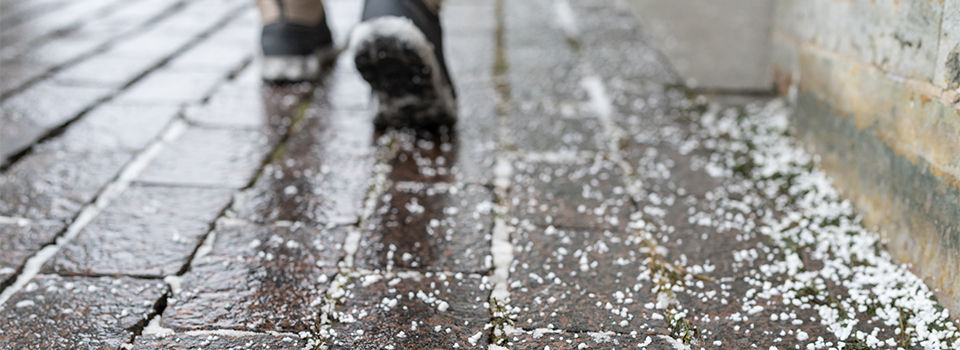 Selective focus on technical salt grains on icy sidewalk surface in wintertime, used for melting ice and snow. Applying salt to keep roads clear and people safe in winter weather from ice or snow