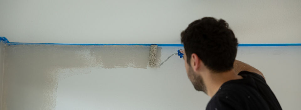 man using paint roller and painting wall with gray paint