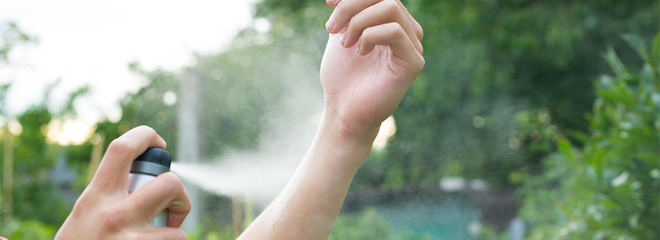 A person spraying insect repellent on their arm