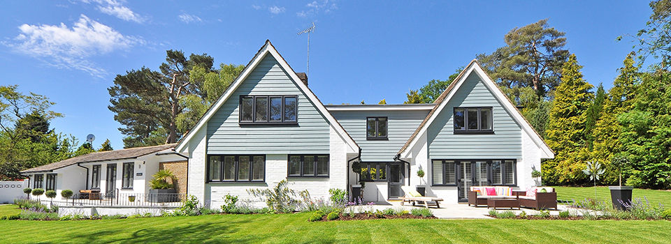 A modern style family home with two peaks. There are many windows that are framed with black trim. The house also had a light blue siding and white brick