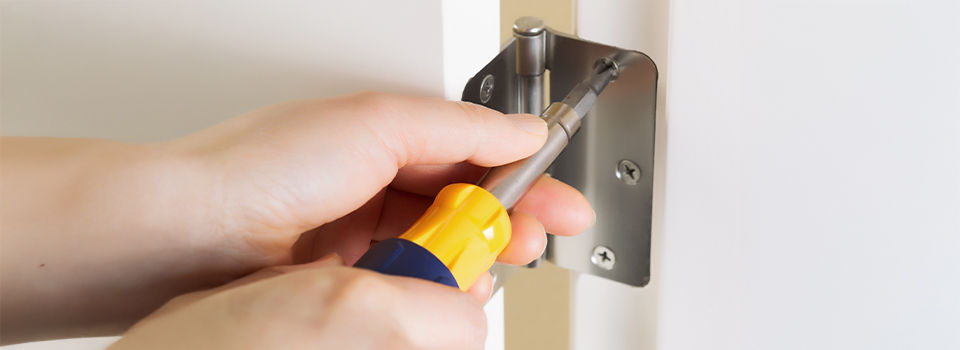 Photo of female hands, with screwdriver, tightening door hinge