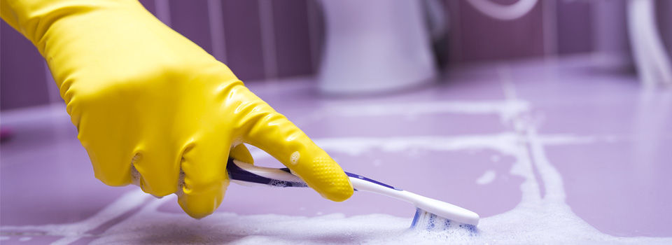 person cleaning grout with gloves on and a toothbrush