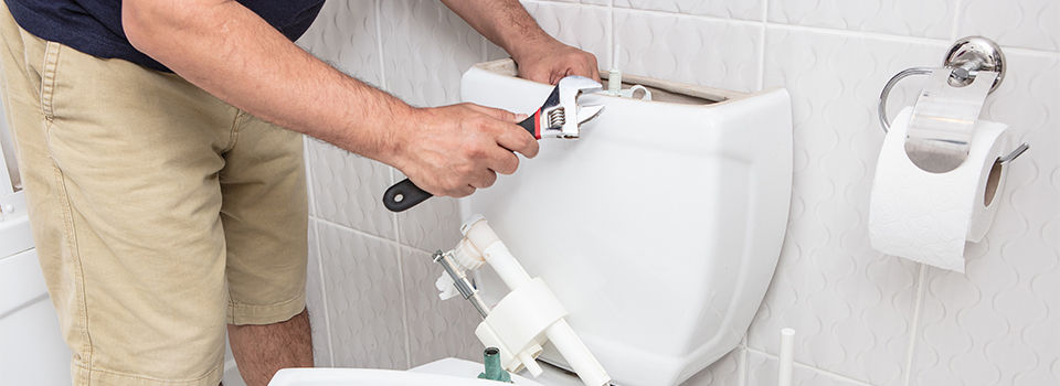 Man using wrench repairing toilet cistern in a concept of DIY repairs with copy space