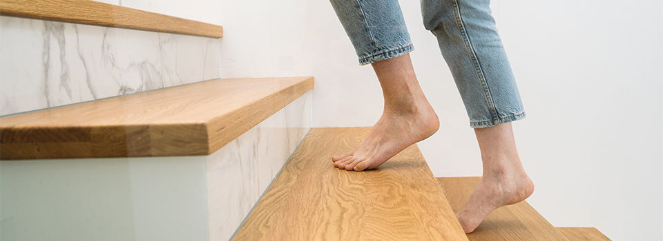 Barefoot woman standing on a wooden staircase at home. Cropped shot of female walking upstairs in apartment. Person climbing on stairs in building