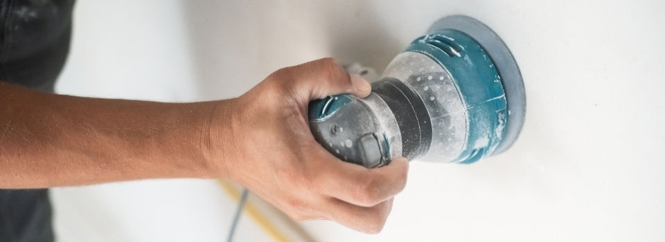 Sanding tool operating on smooth white wall to prepare for painting