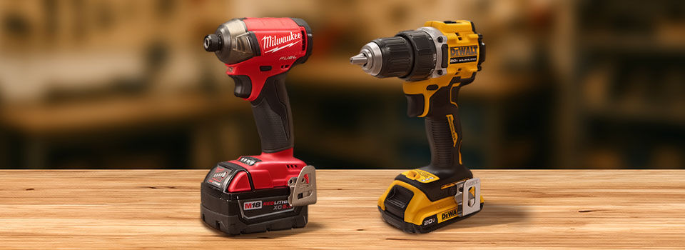 DEWALT ATOMIC 20V MAX Brushless 1/2 In. Compact Cordless Drill and Milwaukee M18 FUEL SURGE Brushless 1/4 In. Hex Hydraulic Cordless Impact Driver on top of wooden workbench table in workshop background