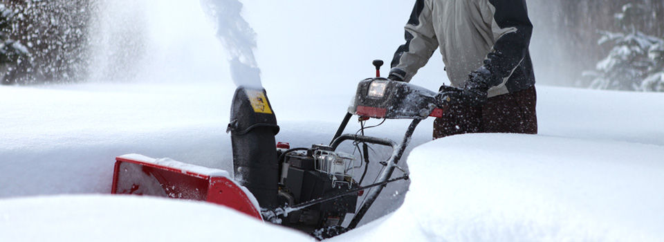 man in goggles pushing a snow blower