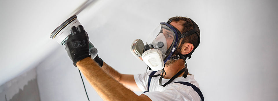 Man wearing dust mask while sanding wall
