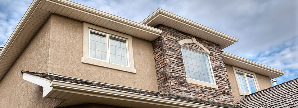 Roofline showing windows, brick stones, gutter, soffit, stucco against blue sky