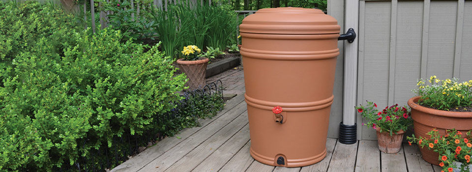 Tan rain barrel connected to a gray downspout for water collection. 