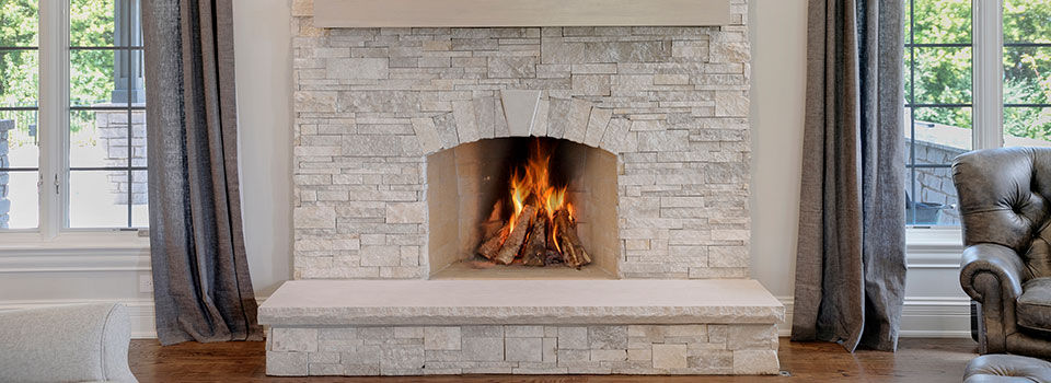 Light grey stone living room fireplace with a fire going inside