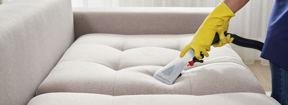 Person wearing yellow cleaning gloves cleaning the couch in a living room