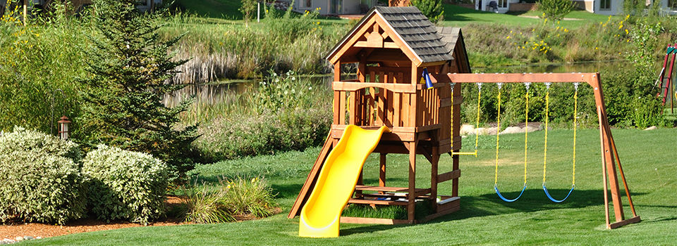 A wooden backyard playset with a yellow slide and two swings 