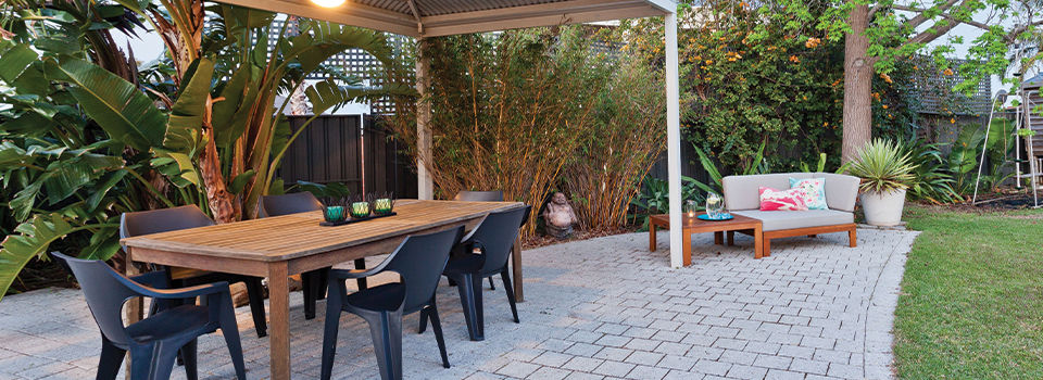 A warm and inviting tropical backyard patio with a wooden table and black chairs.