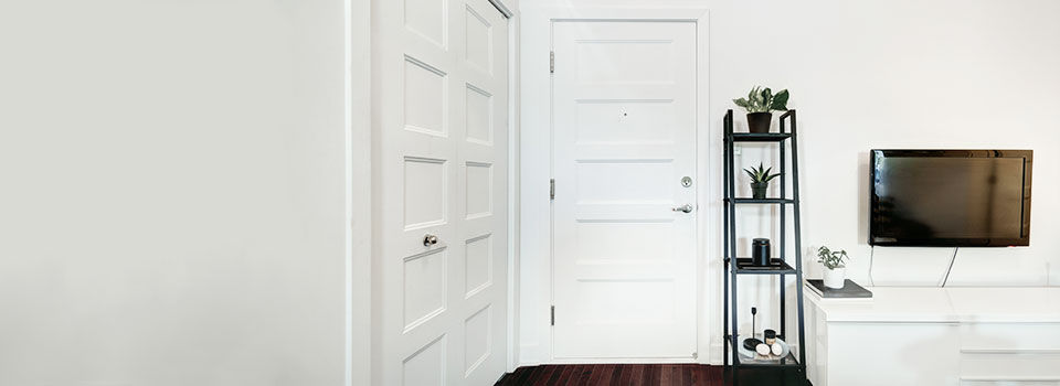 Two solid white doors in a modern style living room with white walls and a black ladder shelf and tv hanging on the wall