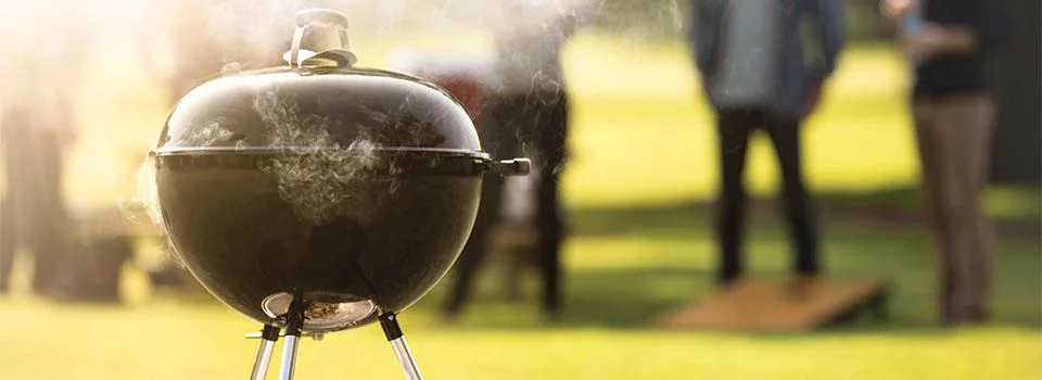 Featuring a charcoal grill with people in the background having a cookout