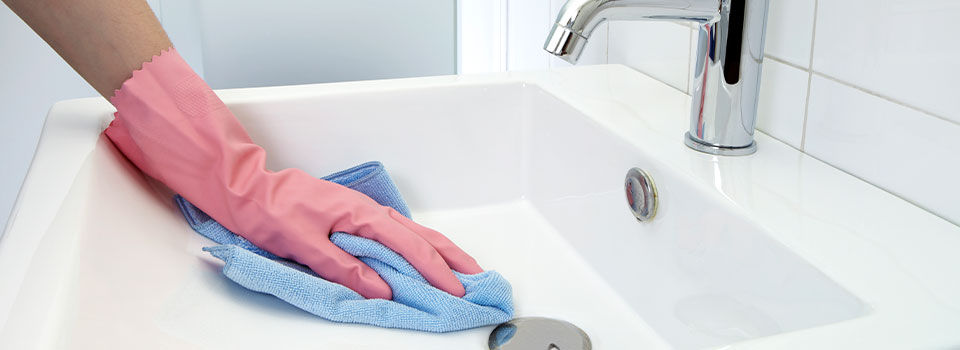 The woman, who is cleaning the washbasin with microfiber cloth and gloves