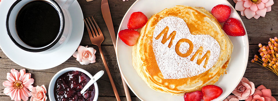 Pancakes with MOM sprinkled in powered sugar surrounded by strawberries and coffee 