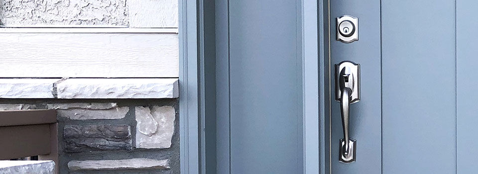 A close up image of a silver door handle on a blue front door with white brick siding