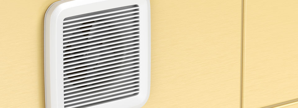 A close up image of a white bathroom exhaust fan mounted on a yellow tiled wall in a bathroom