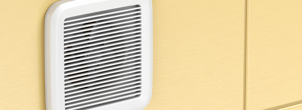 A white, square bathroom exhaust fan is mounted on a yellow tile wall.