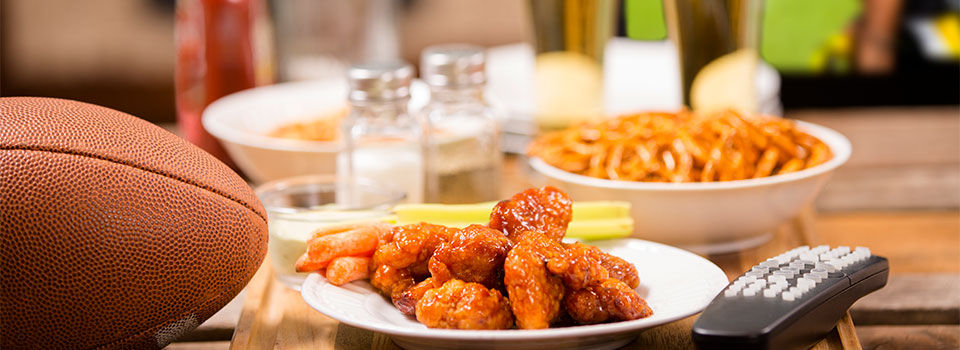 Football, party food, tv remote, salt and pepper sitting on a wooden table ready to watch football