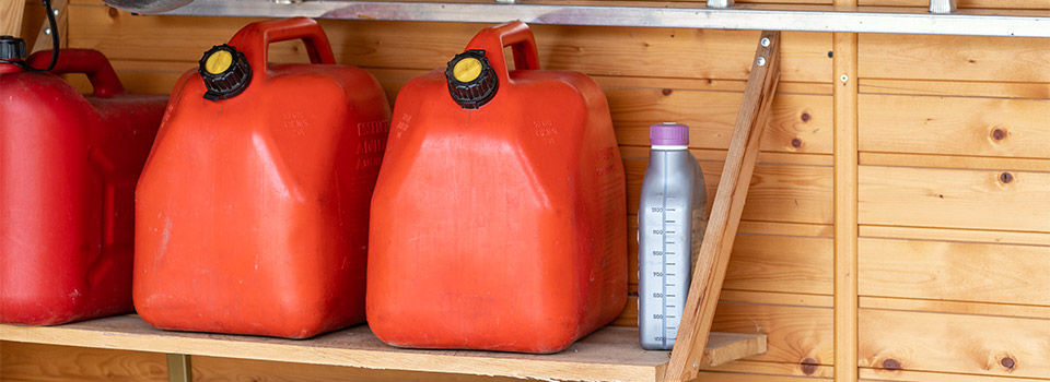Two gas cans sitting next to a can of oil in a garage on a wooden shelf