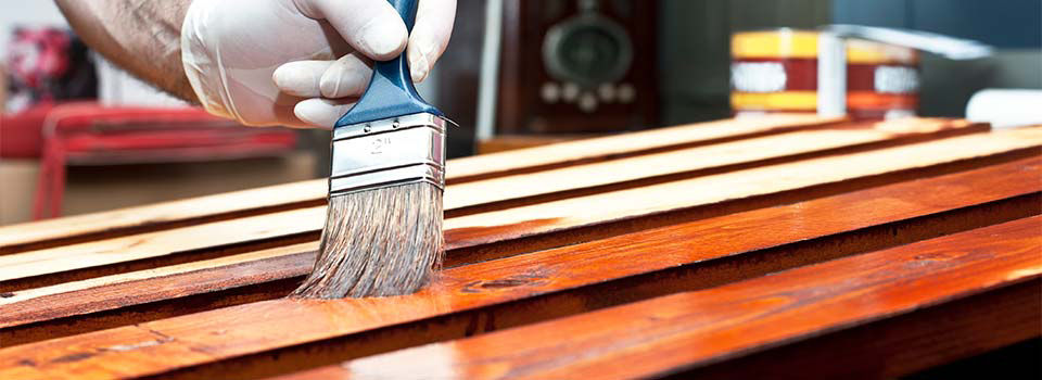 Man wearing a latex glove while brushing on gel stain with a paint brush