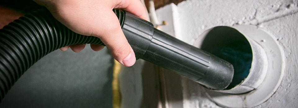 Man's hand holding vacuum hose and cleaning dryer vent