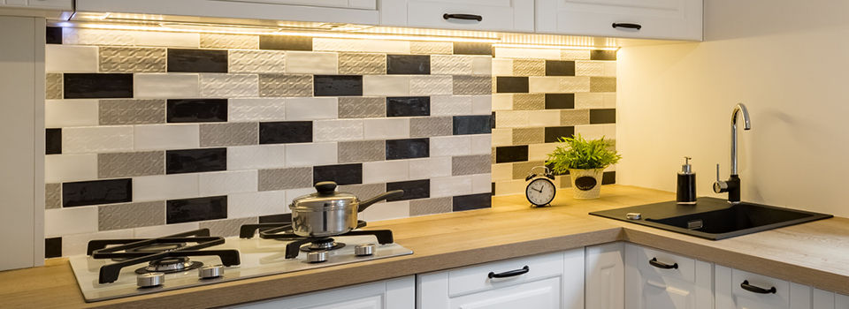Kitchen counter backsplash made from textured tan, black, and white subway tiles with under-cabinet lighting