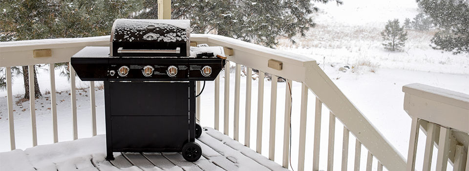 A gas grill on a porch in the winter covered in snow