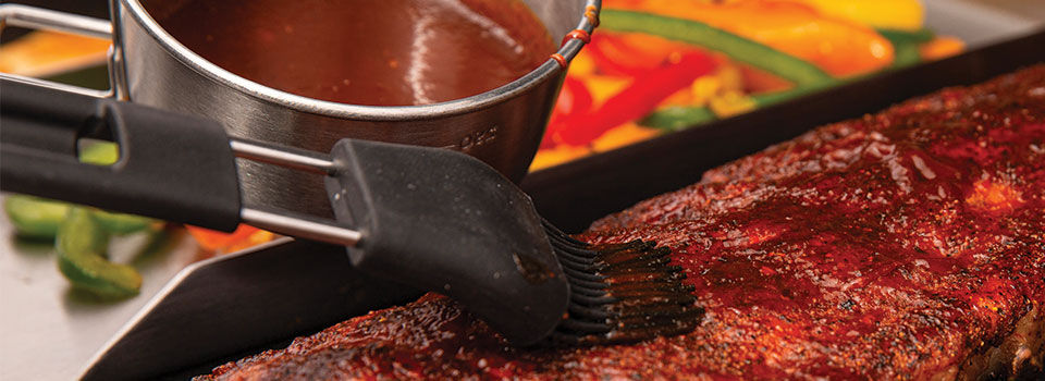 A close up of a person using a basting brush to rub bbq sauce onto a rack of ribs