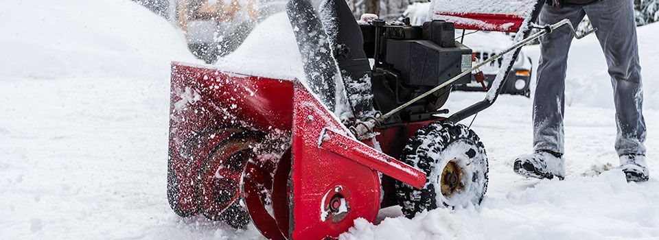 A middle aged man using a red gas powered snow blower to clear his driveway of snow