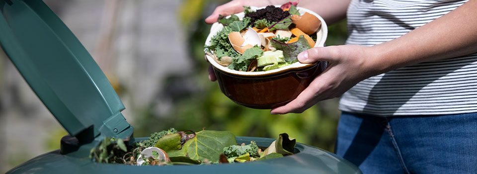 Close Up Of Woman Emptying Food Waste Into Garden Composter At Home