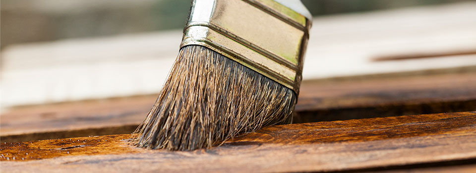 Person using an old paint brush to stain a piece of wood